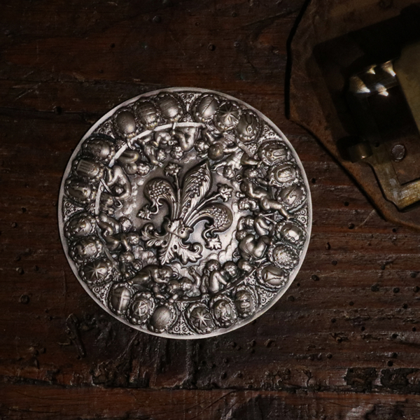 collegamento bassorilievi <p>Silver medal with the Florentine lily in the centre surrounded by cherubs holding the traditional coats of arms of the Arts and Corporations. It was inspired by Vasari's "Apotheosis of Cosimo I", located in the Salone dei Cinquecento in Palazzo Vecchio in Florence.